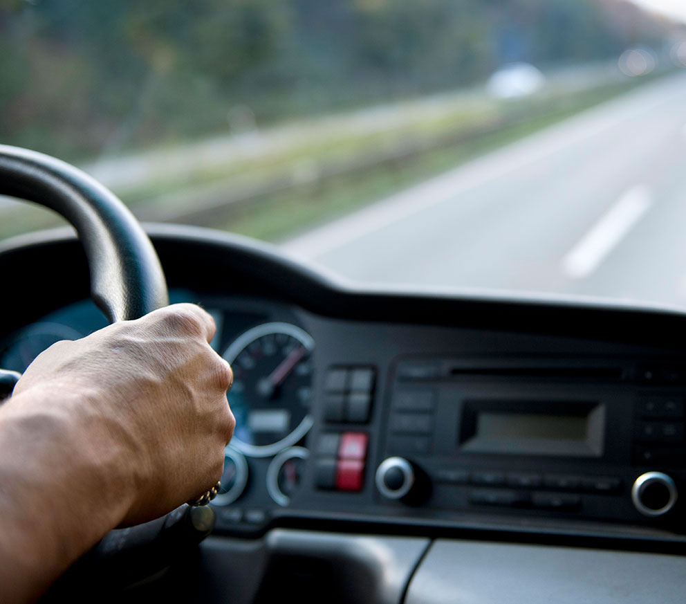 A truck driver inside a cab driving down the highway.