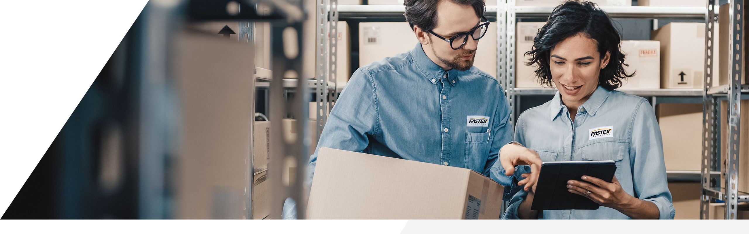 Two Fastex employees viewing a tablet together while in a warehouse holding a package.